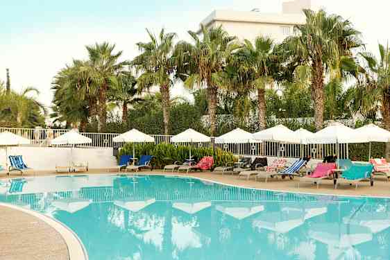 Udendørs pool med liggestole og parasoller omgivet af palmer. (AI-genereret tekst)