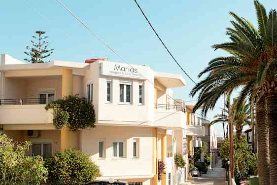 Udvendigt billede af en bygning med skiltet "Marias Studios & Apartments" og tropiske planter i omgivelserne. (AI-genereret tekst)