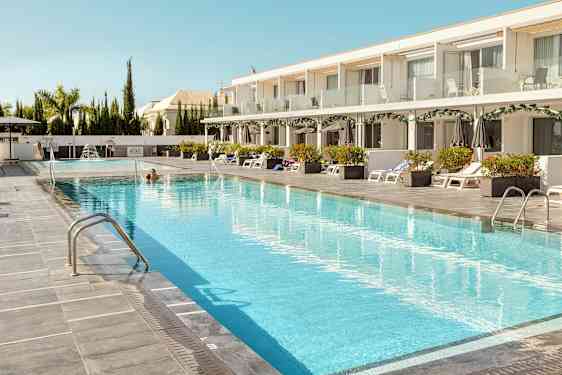 En hotelpool med liggestole og parasoller ved siden af. (AI-genereret tekst)