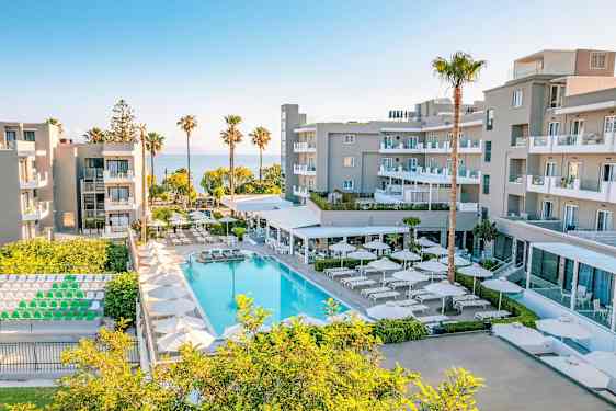 Et moderne hotelkompleks med pool, liggestole og parasoller, omgivet af grønne områder og med udsigt over havet. (AI-genereret tekst)