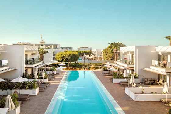 Hotelområde med en lang pool omgivet af liggestole og parasoller, med hvide bygninger i baggrunden. (AI-genereret tekst)