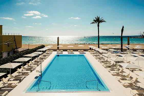 En pool omgivet af liggestole og parasoller tæt på en sandstrand og hav. (AI-genereret tekst)