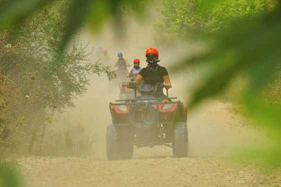 Personer, der kører firhjulede køretøjer på en støvet grusvej omgivet af vegetation. (AI-genereret tekst)