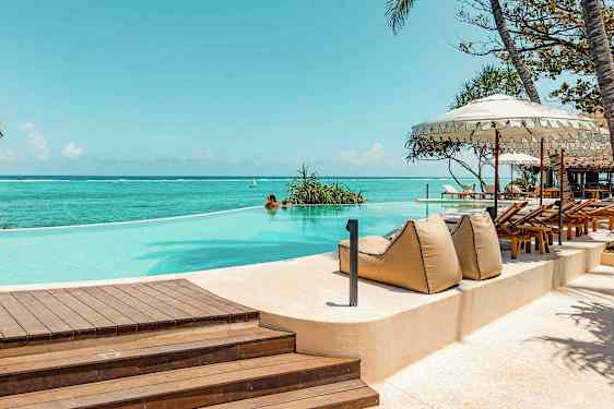 En infinity-pool ved havet, omgivet af liggestole og parasoller. (AI-genereret tekst)