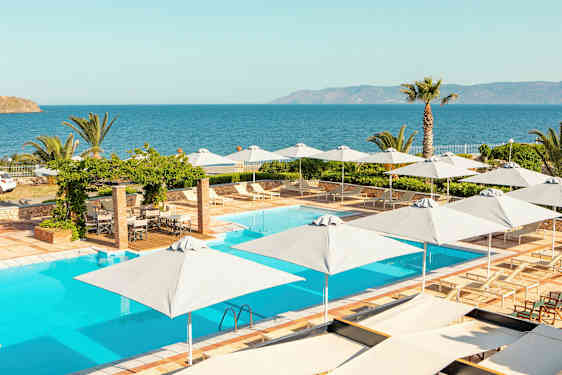 En pool med liggestole og parasoller, udsigt til havet med vegetation omkring. (AI-genereret tekst)