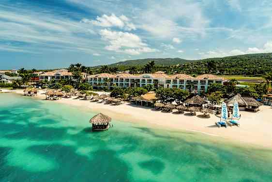 Resort ved strand med grøntblåt vand, palmer og bygninger. (AI-genereret tekst)