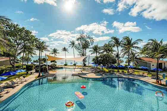 En swimmingpool omgivet af liggestole og parasoller med udsigt over havet og palmer under en klar himmel. (AI-genereret tekst)