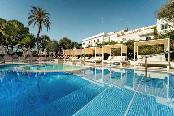 Billede af en pool med turkis vand samt hvide solsenge under parasoller og cabanas. Der er omkringliggende grønt og en skygge af bygninger i baggrunden. (AI-genereret tekst)