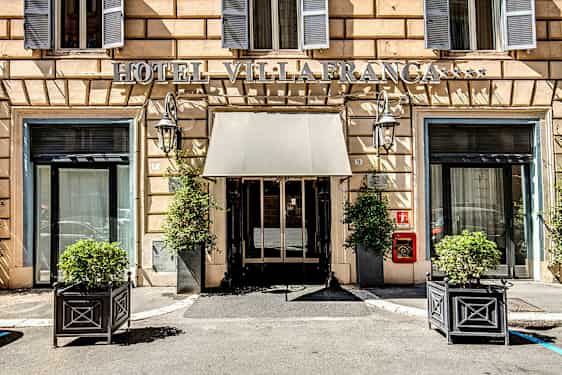 Hotelindgang med skilt, vinduer og planter i potter. (AI-genereret tekst)