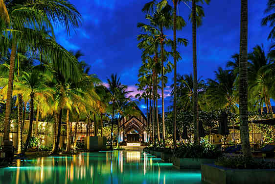 Et aftensbillede af en oplyst pool og høje palmer ved en resort. (AI-genereret tekst)