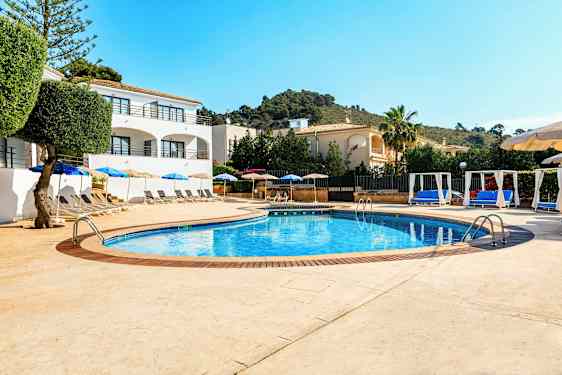 Poolområde med liggestole og parasoller samt omkringliggende bygninger. (AI-genereret tekst)