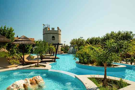 En udendørs pool med liggestole og parasoller samt en stenbygning i baggrunden. (AI-genereret tekst)