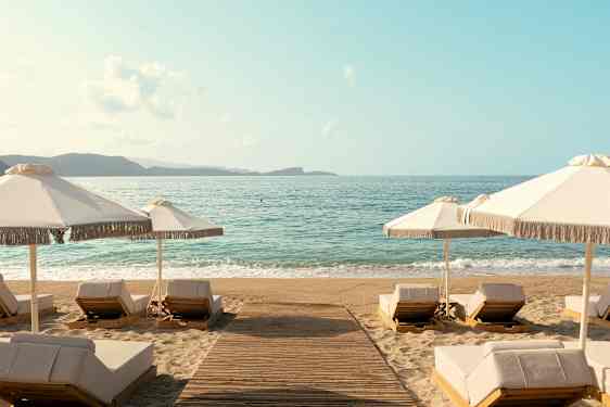 Strand med liggestole og parasoller ved vandkanten. (AI-genereret tekst)