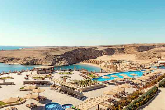 Udsigt over en strand med parasoller og liggestole samt en pool ved siden af havet. (AI-genereret tekst)