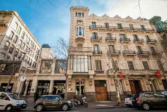 En gade med klassiske bygninger og parkerede biler. Vinduer og altaner pryder facaden. (AI-genereret tekst)