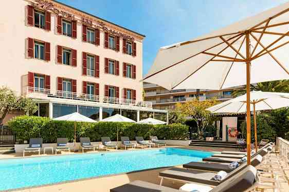 Hotelbygning med pool og liggestole foran. (AI-genereret tekst)