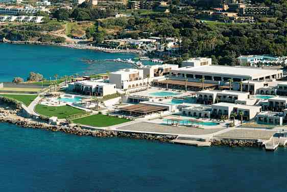 Luftfoto af et hotelkompleks ved kysten med pools og grønne områder. (AI-genereret tekst)