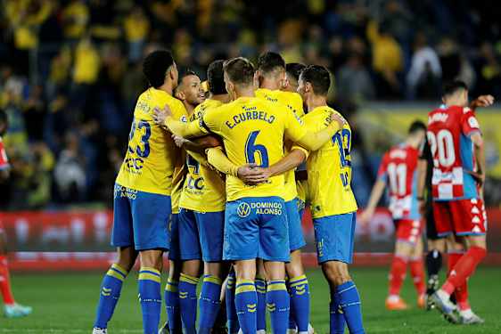 Fodboldspillere i gule trøjer krammer hinanden på banen. (AI-genereret tekst)