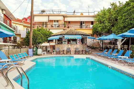 En udendørs swimmingpool omgivet af liggestole og parasoller, med en lille café i baggrunden. (AI-genereret tekst)