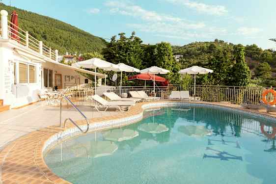 Udendørs swimmingpool med liggestole og parasoller ved en terrasse nær grønne områder. (AI-genereret tekst)