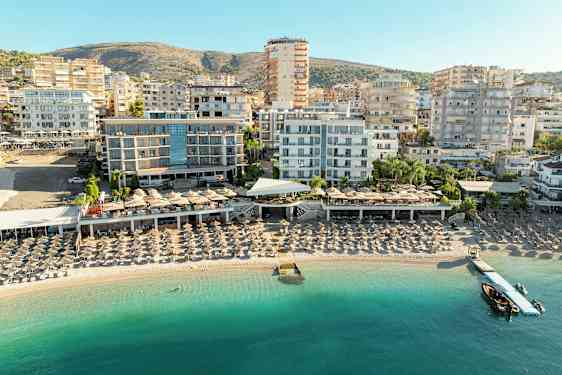 Udsigt over strand med liggestole og hotelbygninger i baggrunden. (AI-genereret tekst)