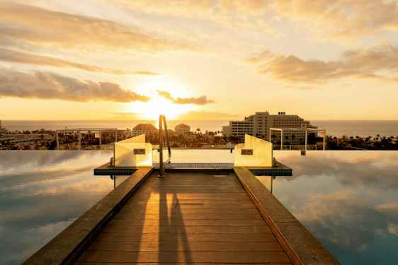 En infinitypool med træbro og udsigt over havet ved solnedgang. (AI-genereret tekst)