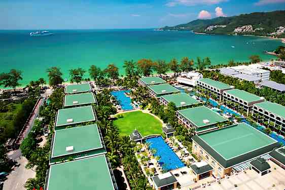 Luftfoto af et feriehotel med flere bygninger omgivet af grønne områder og swimmingpools, beliggende ved havet. (AI-genereret tekst)