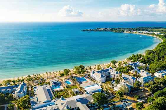 Billede af en kyststrækning med turkis vand, en hvid sandstrand og hotelbygninger i nærheden. (AI-genereret tekst)
