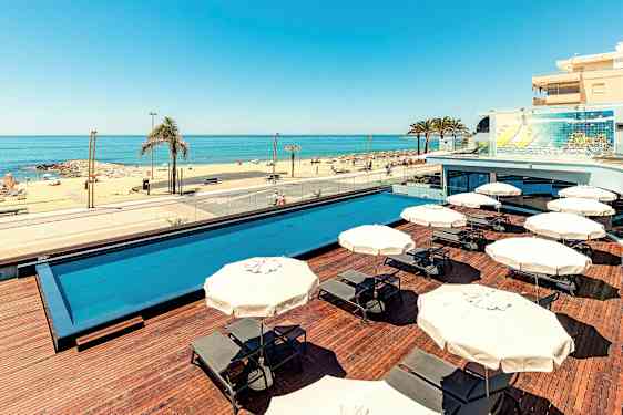 En udendørs pool med liggestole og parasoller, samt en sandstrand med havudsigt. (AI-genereret tekst)