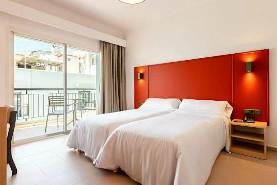 Et værelse med to enkeltsenge med hvidt sengetøj, en rød sengegavl og en balkon udenfor. (AI-genereret tekst)