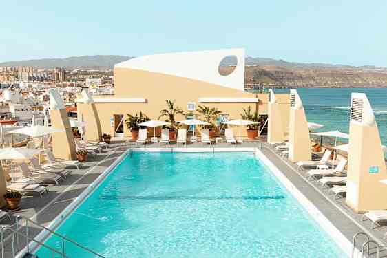 En tagpool omgivet af liggestole og parasoller med udsigt over byen og havet. (AI-genereret tekst)