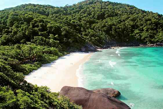 Billede af en strand omgivet af grønne bjerge og blåt hav. (AI-genereret tekst)