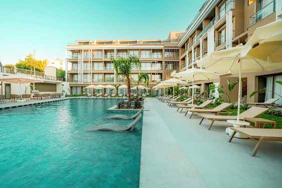 En hotelpool med solsenge og parasoller ved siden af moderne bygninger. (AI-genereret tekst)