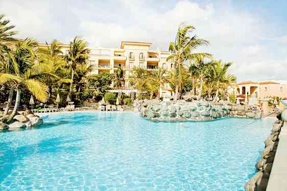 Billede af en pool med palmer og en bygning i baggrunden. (AI-genereret tekst)