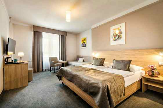 Et hotelværelse med en stor dobbeltseng, et bord med to stole og et vægmonteret TV. (AI-genereret tekst)