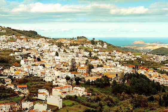 Udsigt over en by med mange hvide bygninger beliggende i en frodig dal nær havet. (AI-genereret tekst)