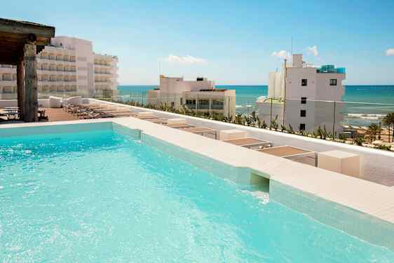 En pool med udsigt til en strand med flere bygninger i baggrunden. (AI-genereret tekst)