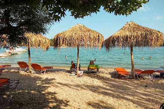 Strand med liggestole og parasoller nær havet, folk svømmer i vandet. (AI-genereret tekst)