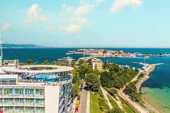 Billede af en kystby med havet i baggrunden. Et stort hus med en pool på taget ses i forgrunden. (AI-genereret tekst)