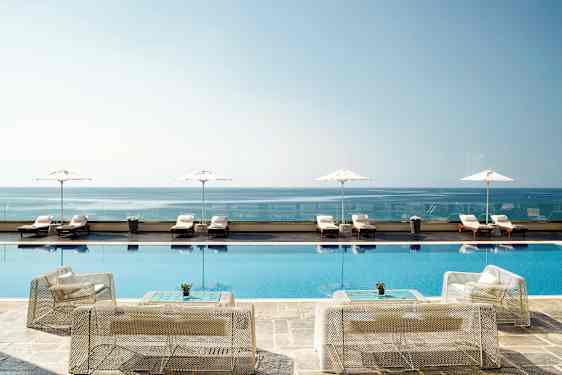 Billede af en infinitypool ved kysten med liggestole og parasoller i baggrunden. (AI-genereret tekst)