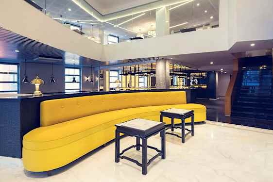 Et stilfuldt indrettet rum med en gul sofa, små borde og moderne belysning. (AI-genereret tekst)