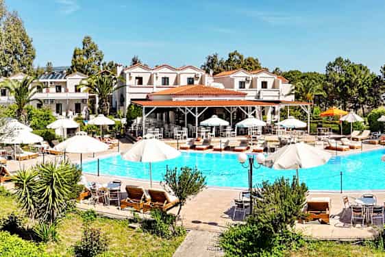 En udendørs pool med liggestole og parasoller, omgivet af grønt og bygninger i baggrunden. (AI-genereret tekst)