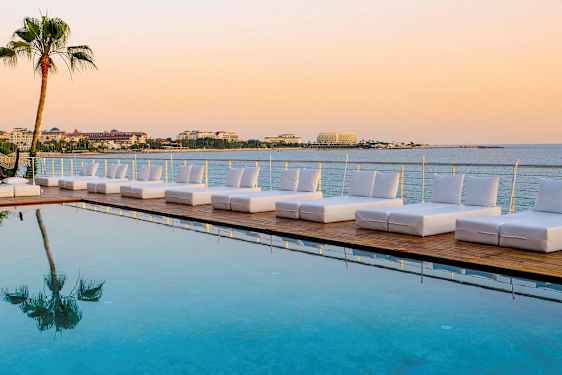 Liggestole ved en pool med udsigt over havet og bygninger i baggrunden. (AI-genereret tekst)