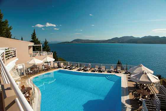 En udendørs swimmingpool med liggestole og parasoller, med udsigt over havet og bjerge i det fjerne. (AI-genereret tekst)