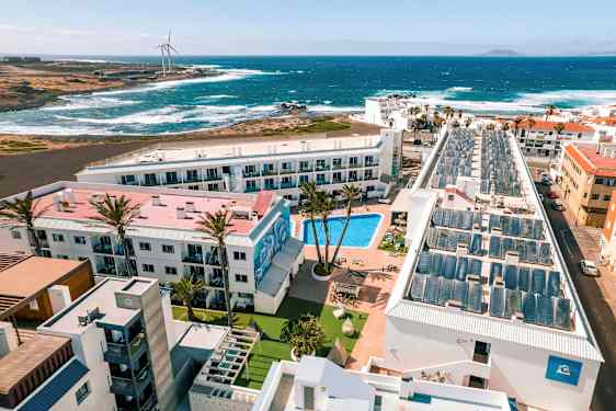 En hotelresort med pool, omgivet af bygninger, med udsigt til havet og bølgerne. (AI-genereret tekst)