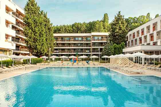 Udendørs swimmingpool med liggestole og parasoller, omgivet af moderne bygninger og grønt. (AI-genereret tekst)