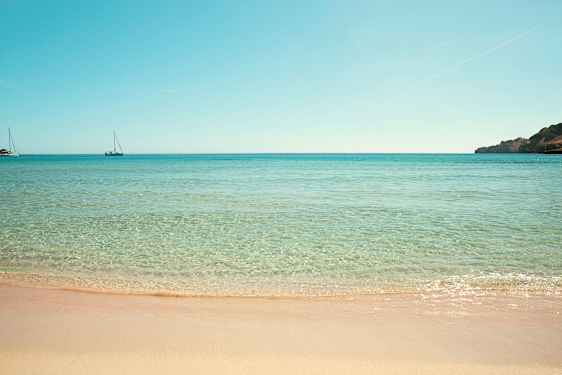 Strand med klart vand og to sejlbåde på havet. (AI-genereret tekst)