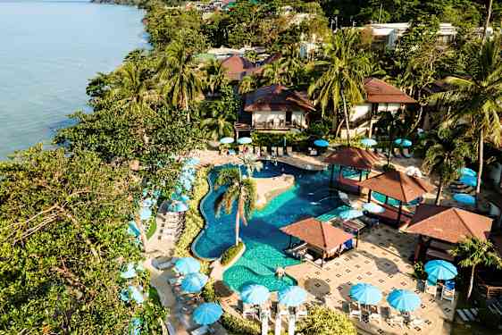 Et feriested med pool, palmer og parasoller ved havet. (AI-genereret tekst)