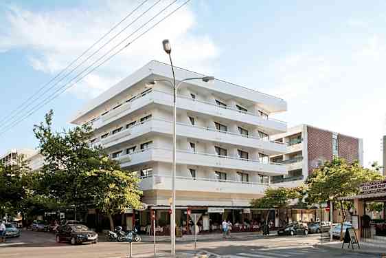 Fire etager højt, hvidt hotel med altaner. Nederst i bygningen er der en restaurant. (AI-genereret tekst)