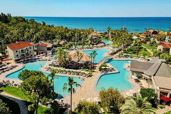 En resort med flere pools omgivet af grønne områder og bygninger med havet i baggrunden. (AI-genereret tekst)